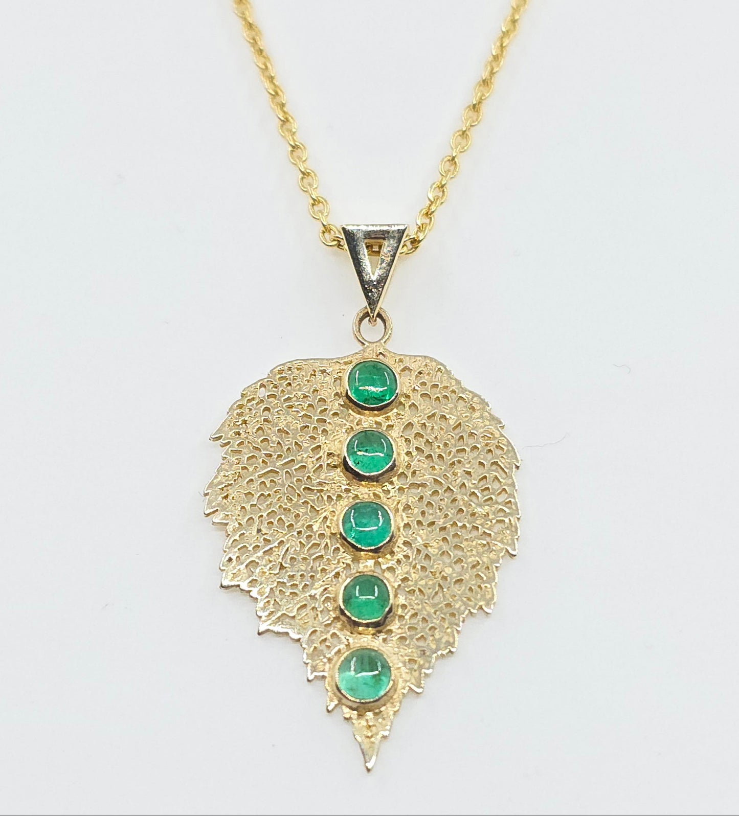 Gold necklace with a leaf-shaped pendant featuring green gemstones on a white background