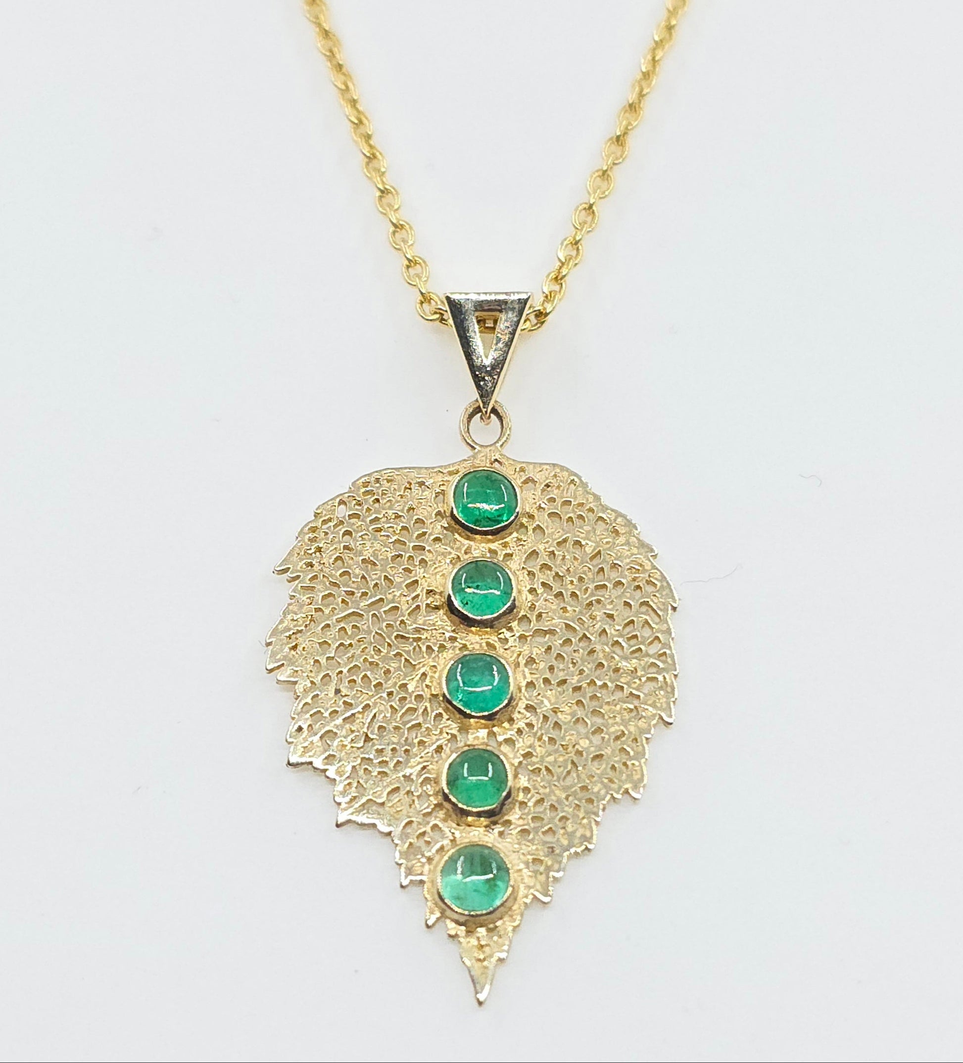 Gold necklace with a leaf-shaped pendant featuring green gemstones on a white background